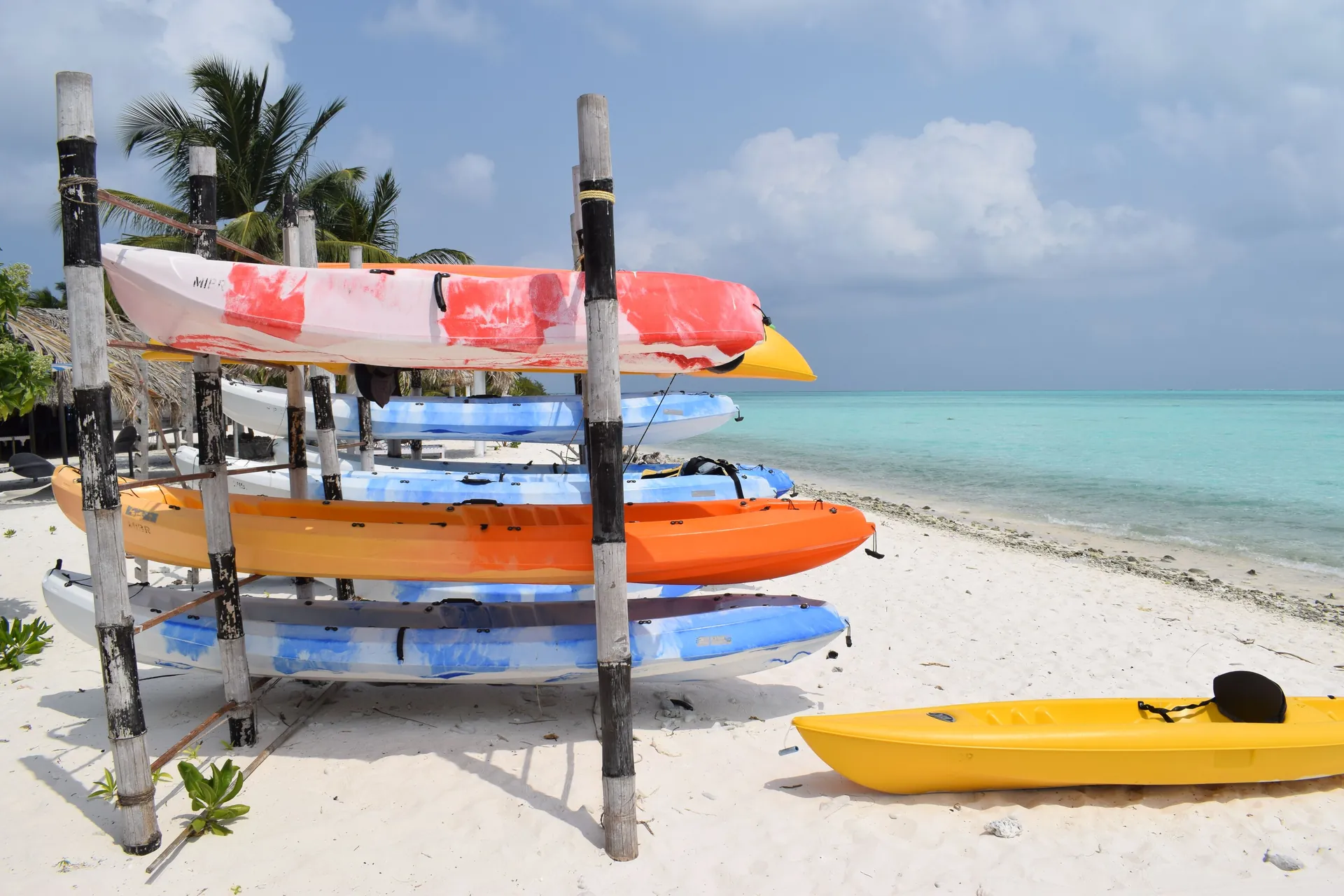 Colorful kayaks stacked on the sandy shores of Minicoy Island, India, with a clear turquoise sea backdrop.
