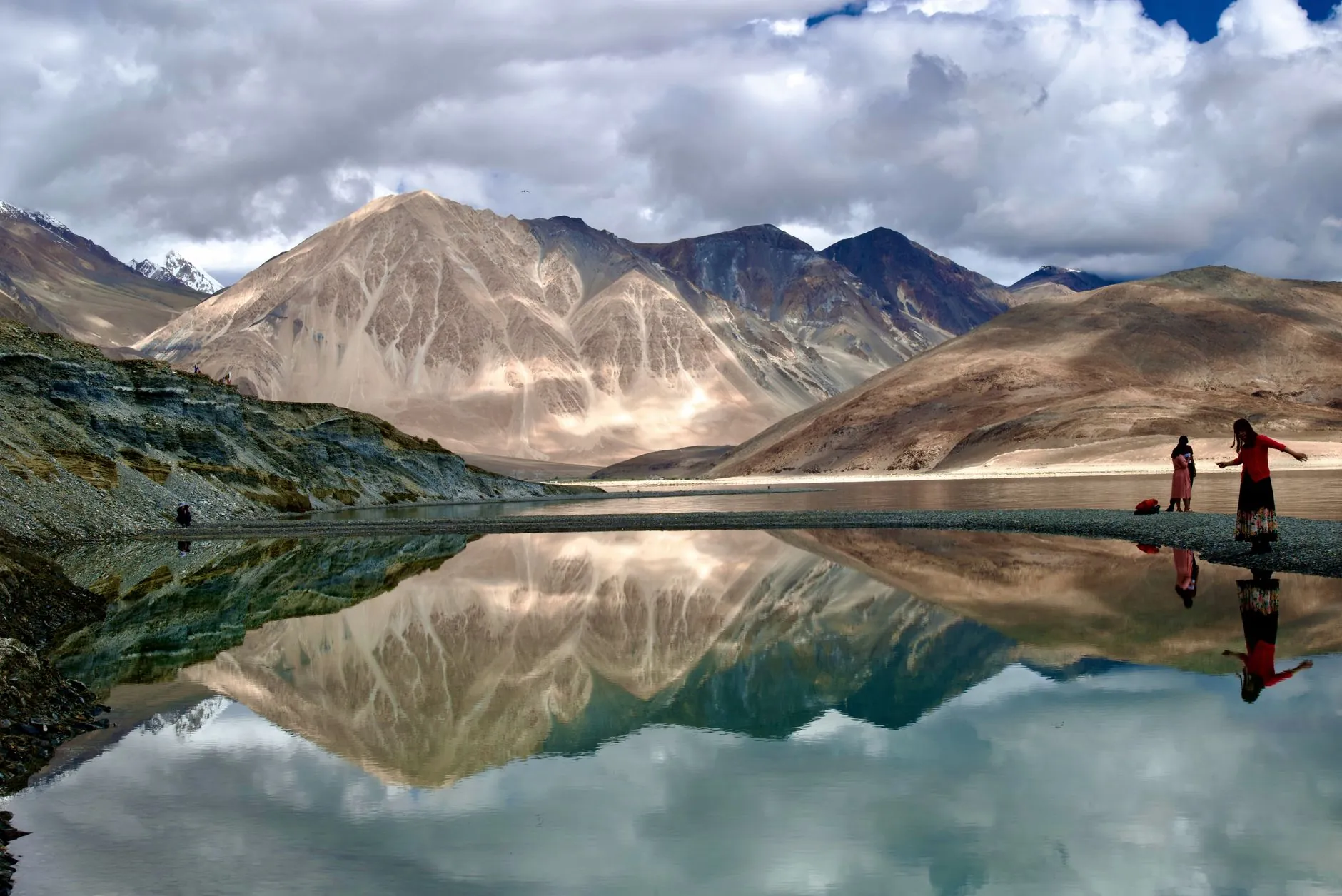 Captivating view of mountains and their reflection in Pangong Lake with people in the scene.