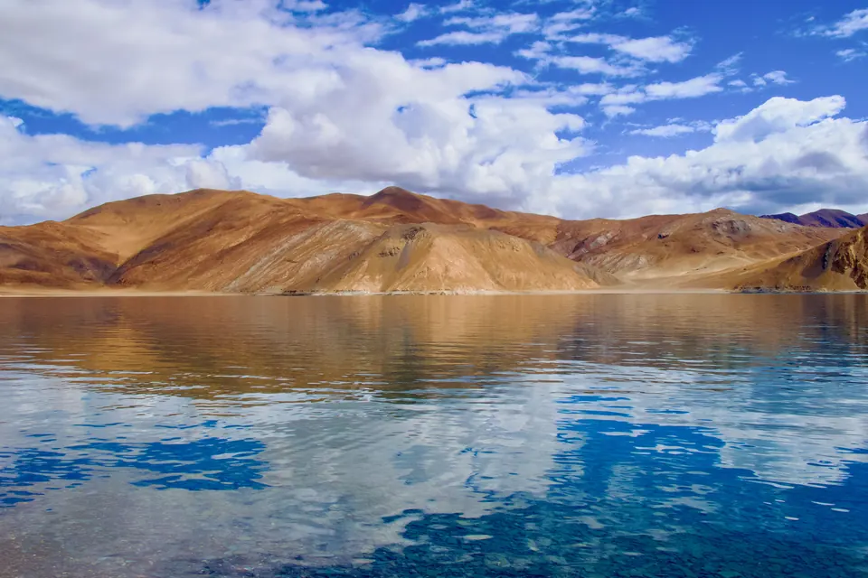 Stunning view of Pangong Tso Lake reflecting arid hills and blue sky. Perfect for travel inspiration.