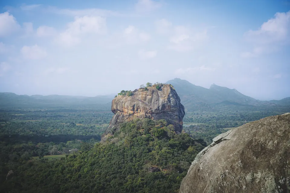 A stunning view of Sigiriya Rock Fortress in Sri Lanka, surrounded by lush greenery under a bright blue sky.