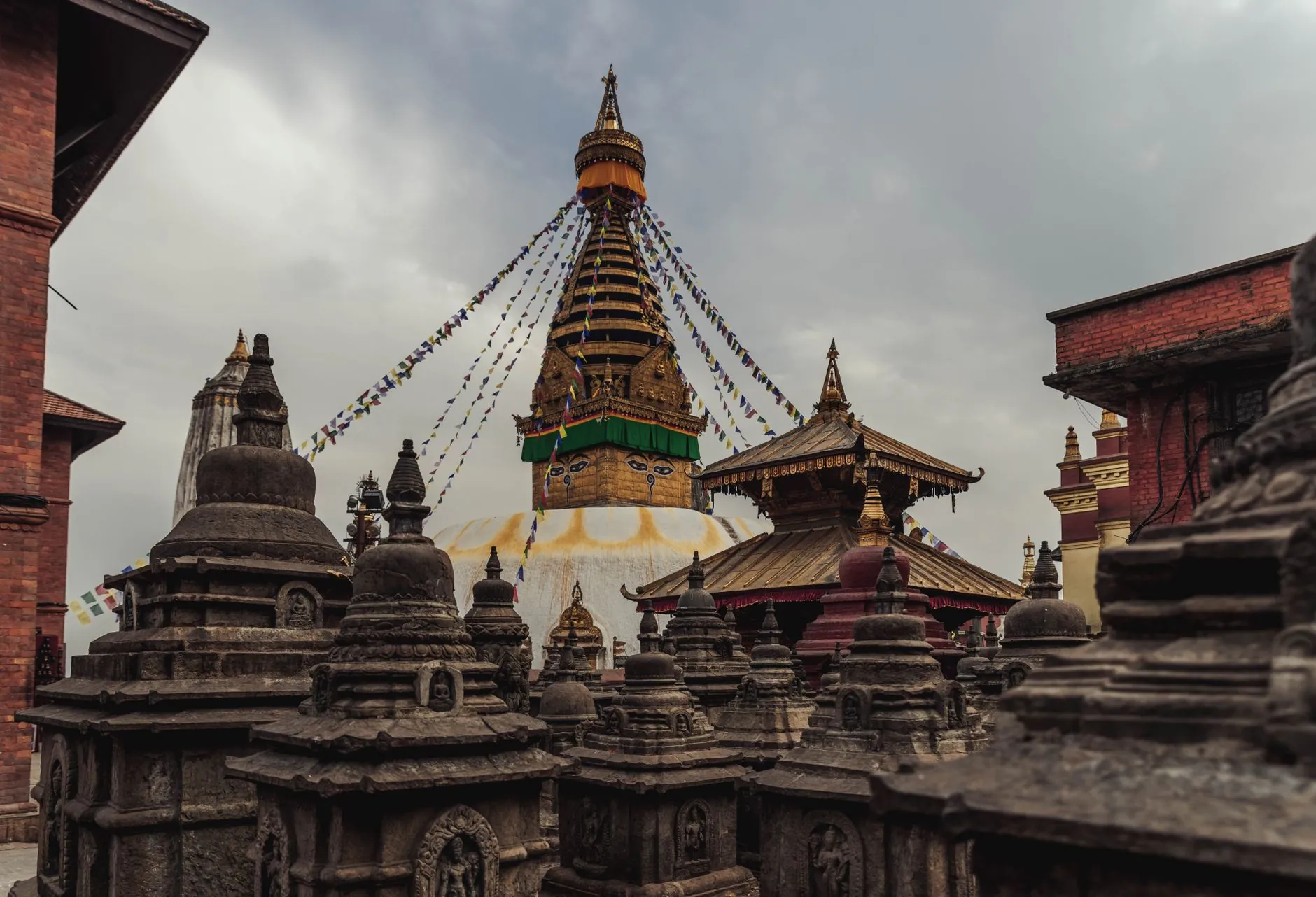 Ancient Swayambhunath Stupa in Kathmandu with vibrant prayer flags under cloudy sky.