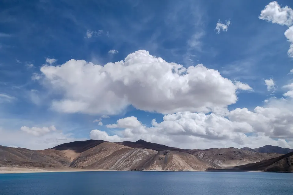 A breathtaking view of Pangong Lake's turquoise waters and dramatic clouds under a clear blue sky.
