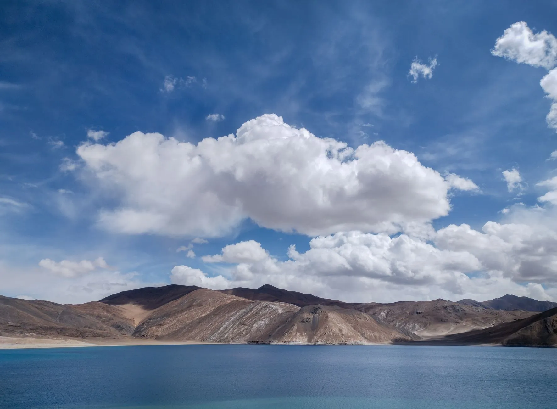 A breathtaking view of Pangong Lake's turquoise waters and dramatic clouds under a clear blue sky.