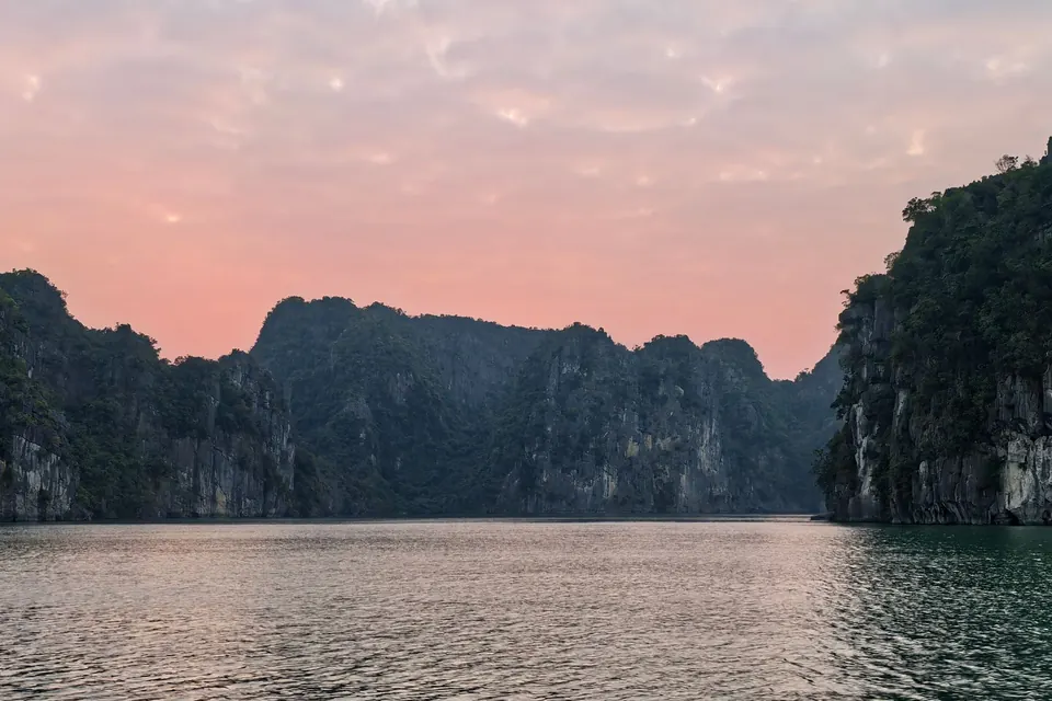Beautiful view of Halong Bay's limestone formations with a pink sunset sky.