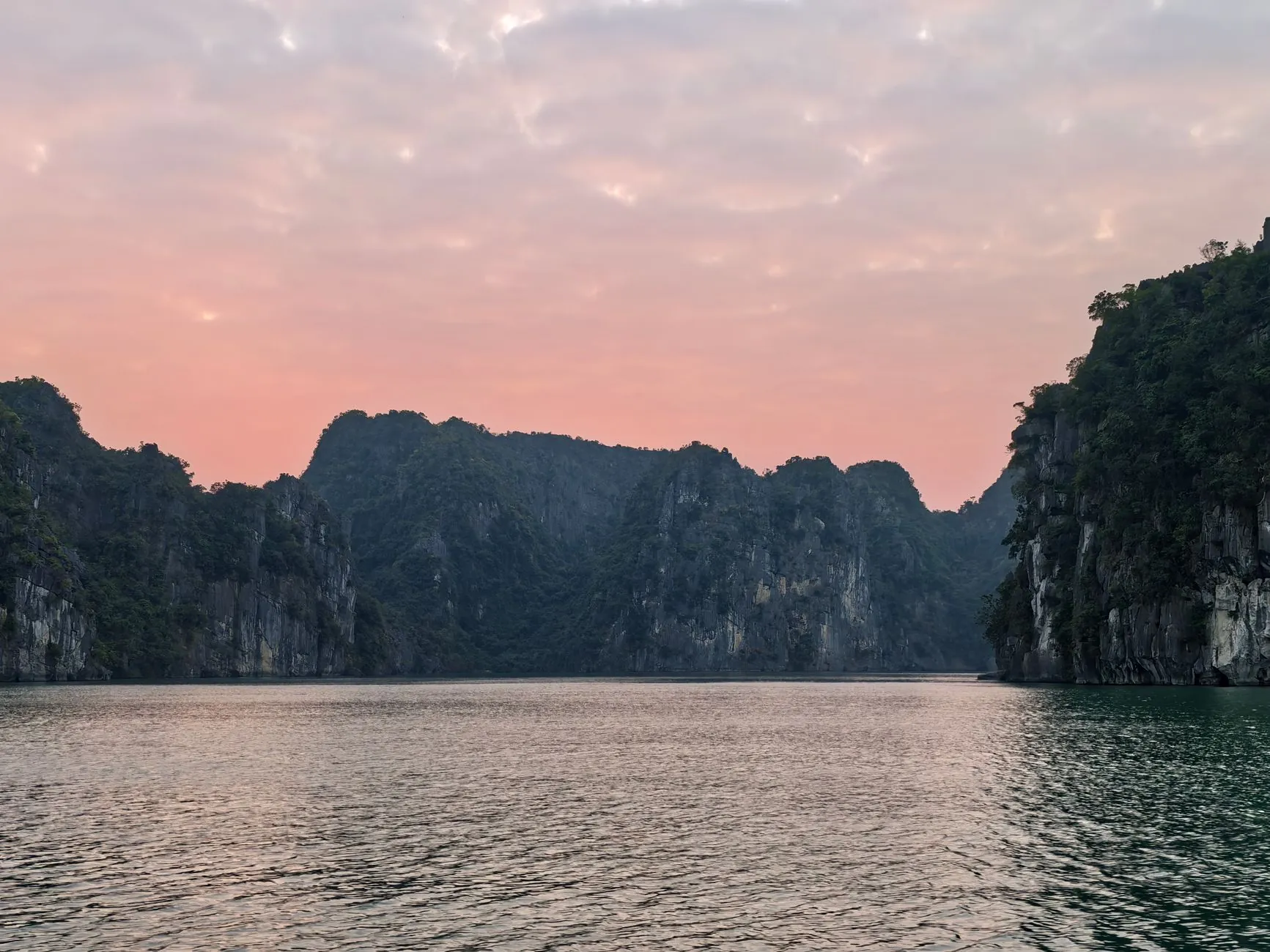 Beautiful view of Halong Bay's limestone formations with a pink sunset sky.