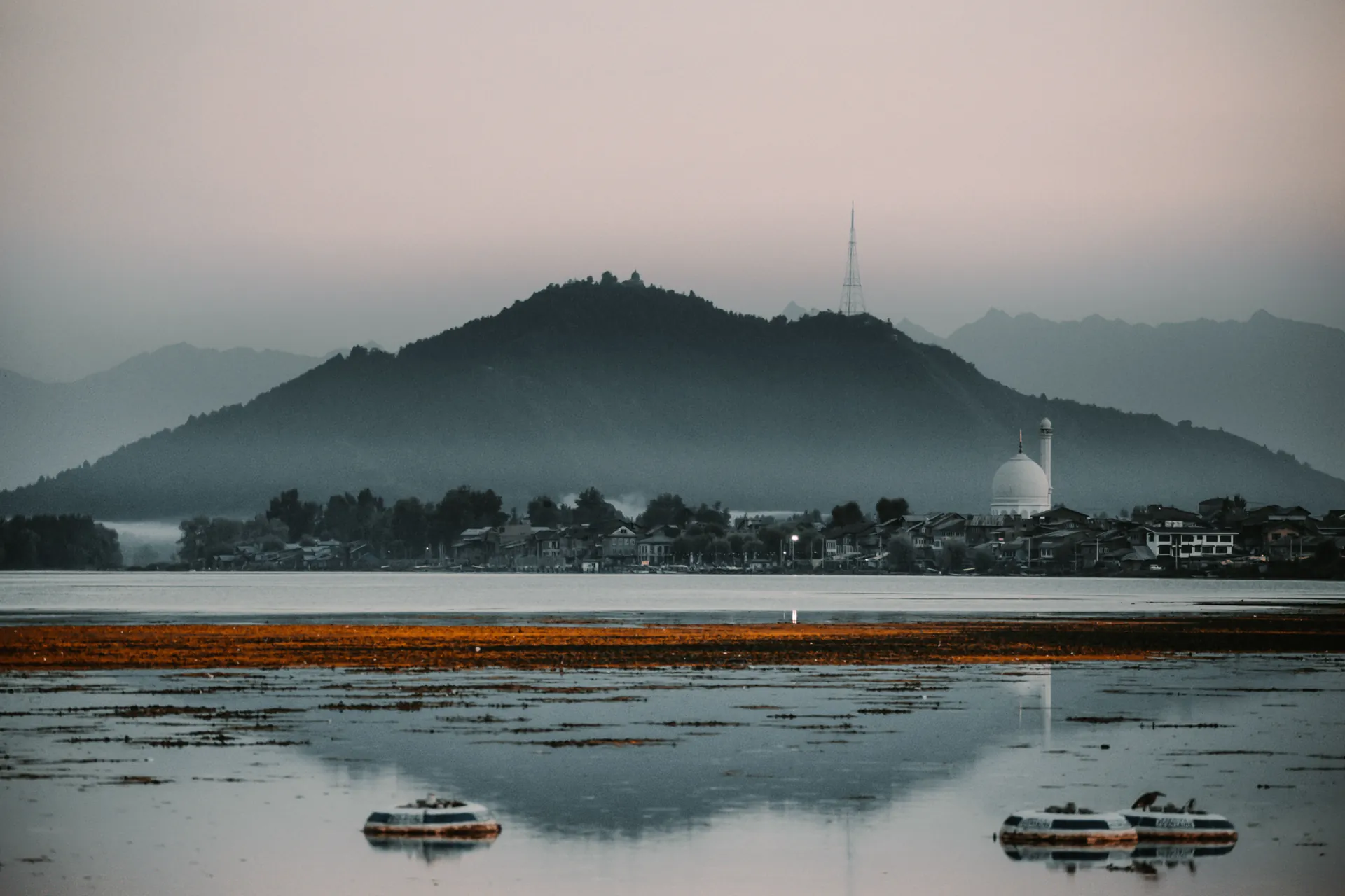 A tranquil view of Dal Lake with Hazratbal Shrine silhouetted against misty mountains in Srinagar, India.