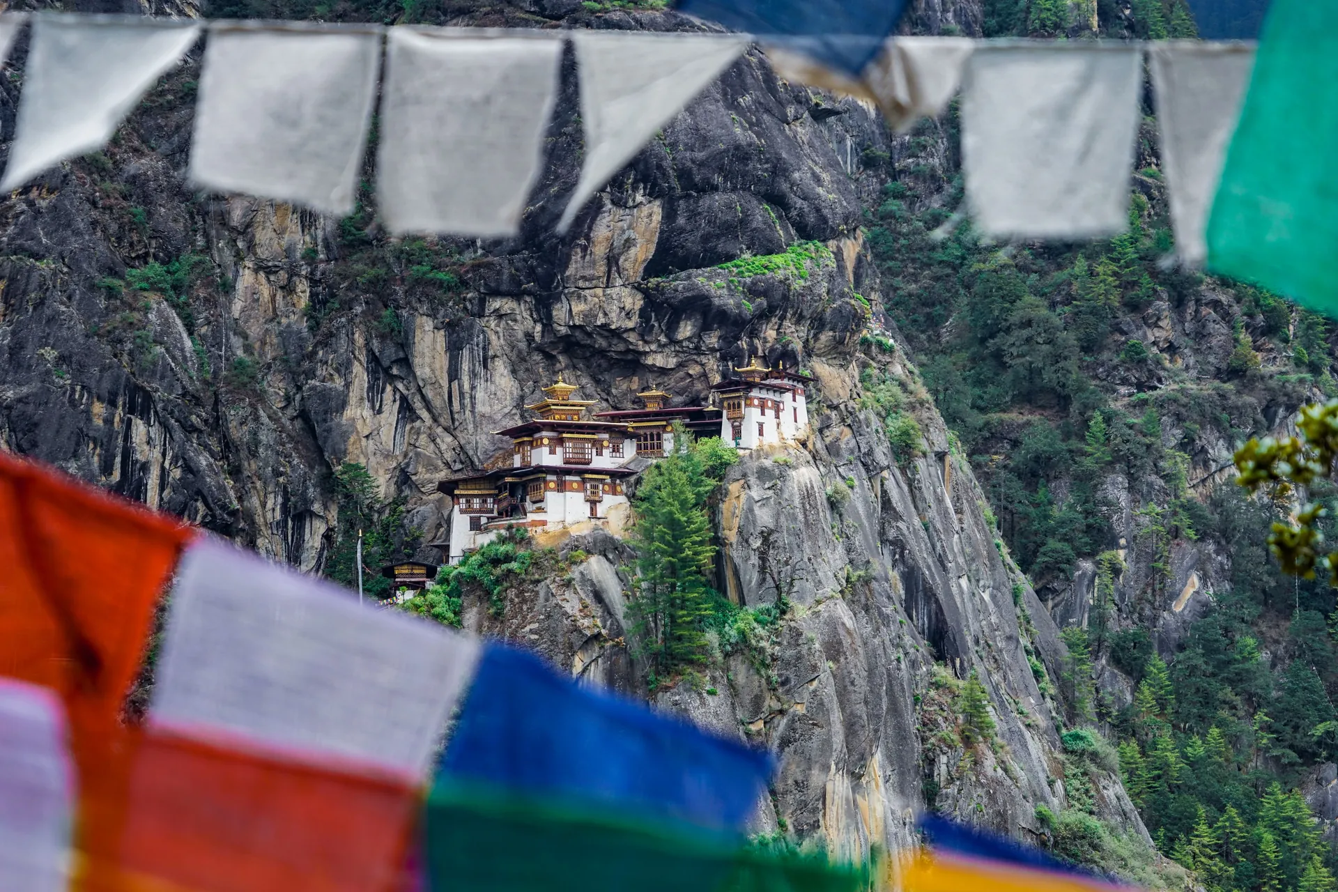A stunning view of Paro Taktsang Monastery nestled in the cliffs of Bhutan with vibrant prayer flags.