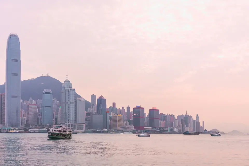 Serene view of the Hong Kong skyline at sunset with boats on Victoria Harbour.